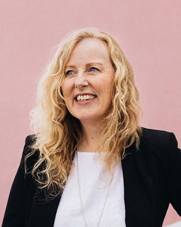Lyn Baird, smiling, in a black jacket and white top.